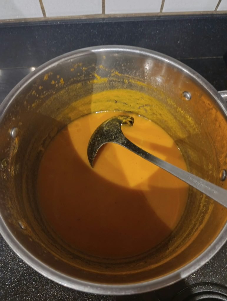 Zoeteaardappelsoep met kokos in een pan met soeplepel