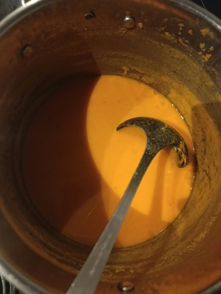Close-up van oranje zoeteaardappelsoep met kokos en een soeplepel in de pan