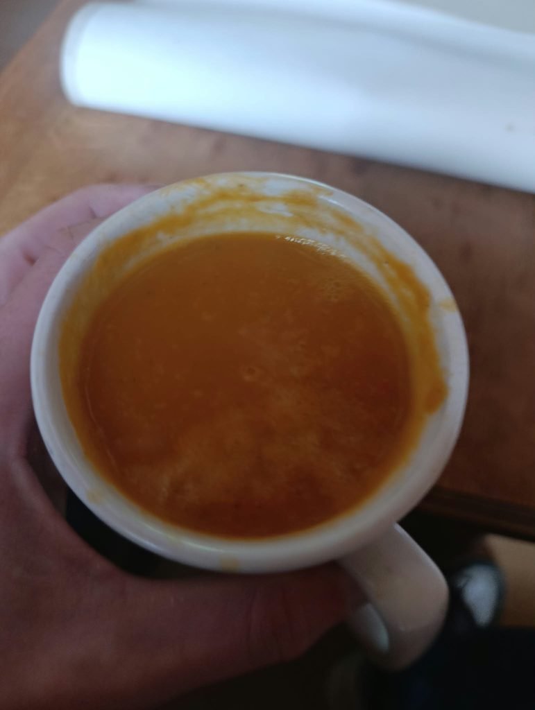Hand met een wit kopje oranje zoeteaardappelsoep met kokos